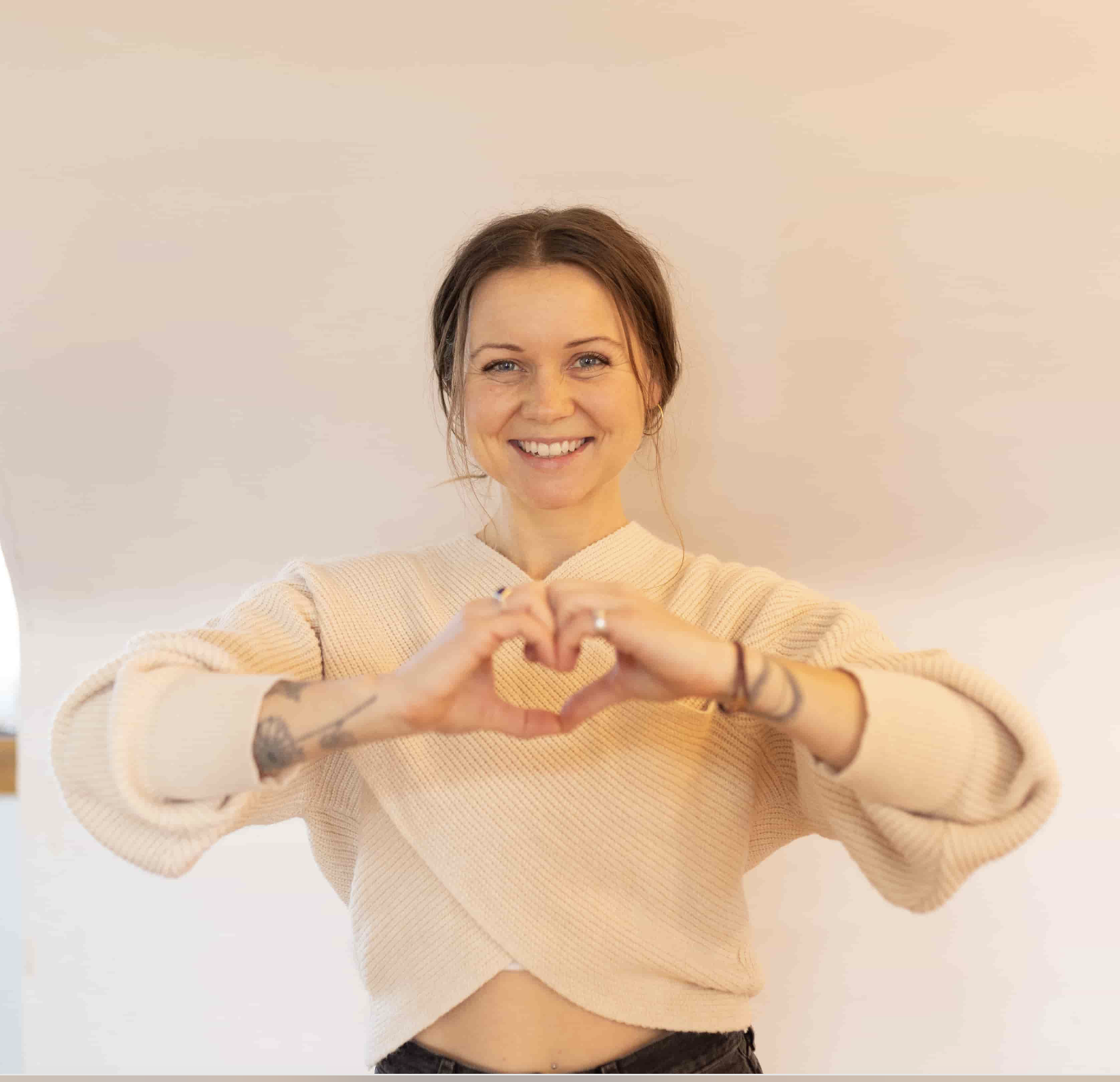 yoga teacher with heart hands smiling in white